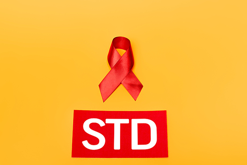 top view of red ribbon as hiv awareness near std lettering isolated on orange
