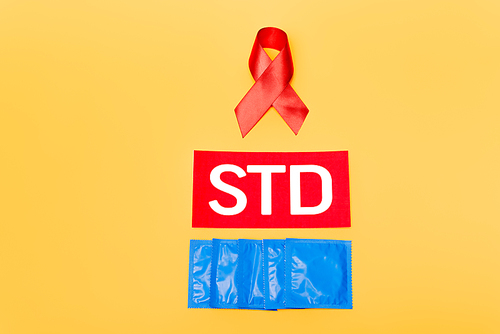 red ribbon as hiv awareness near std lettering and condoms isolated on orange