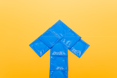 top view of blue arrow from packs with condoms isolated on orange