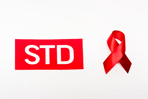 top view of red ribbon near paper with std lettering isolated on white
