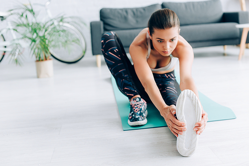 Selective focus of sportswoman stretching leg on fitness mat at home