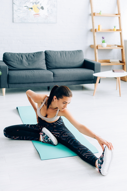 Young woman in sportswear warming up on fitness mat at home