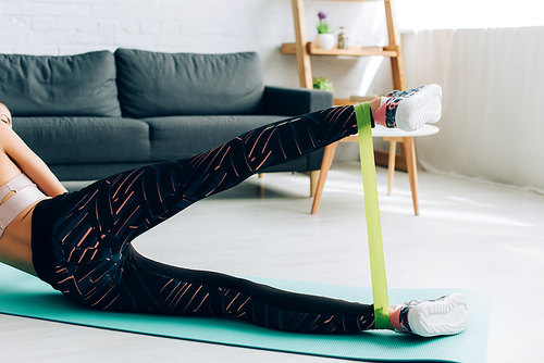 Cropped view of sportswoman working out with resistance band in living room