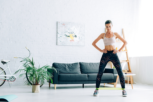 Fit woman in sportswear and sneakers using resistance band while training at home