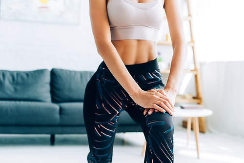 Cropped view of sportswoman putting hands on knee while doing lunges in living room