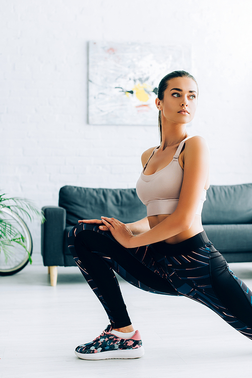 Young sportswoman looking away while doing lunges at home