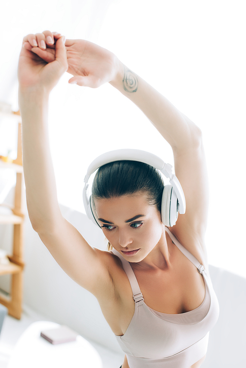Selective focus of brunette sportswoman in headphones working out in living room