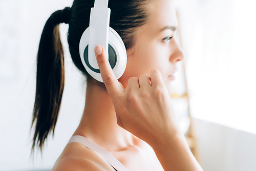 Side view of brunette woman touching headphones at home