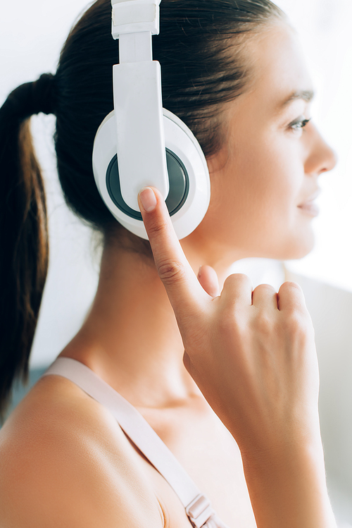 Selective focus of young brunette woman touching headphones while listening music at home