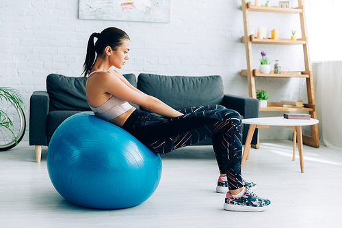 Side view of sportswoman working out on fitness ball in living room