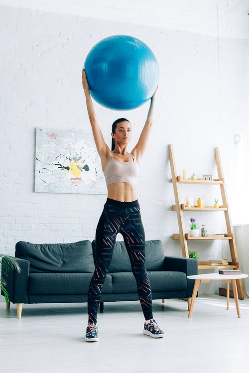 Young sportswoman holding fitness ball in living room