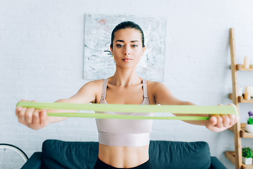 Selective focus of focused sportswoman training with resistance band at home