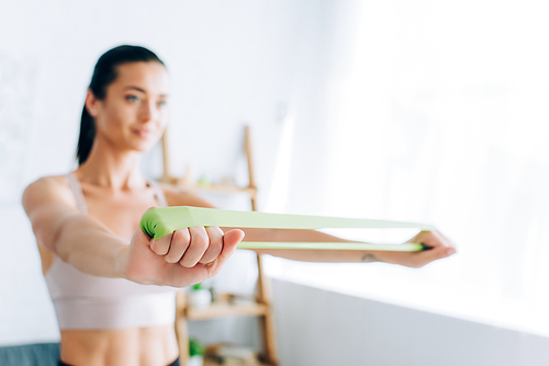 Selective focus of young sportswoman using resistance band while exercising at home