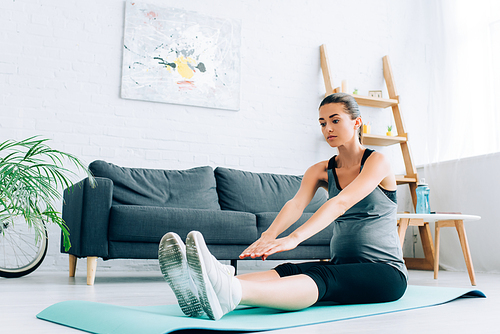 Selective focus of young pregnant sportswoman stretching on fitness mat at home