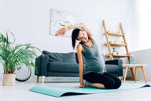 Selective focus of pregnant sportswoman warming up on fitness mat at home