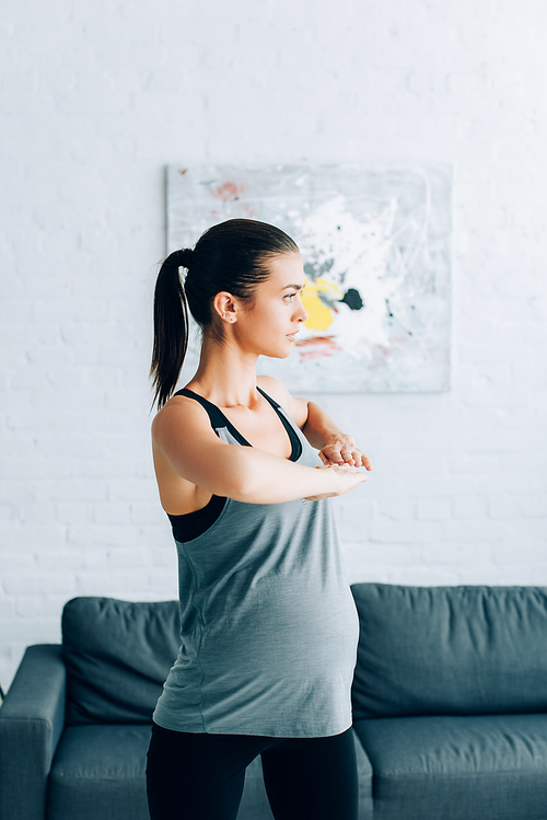 Young pregnant sportswoman looking away while exercising in living room