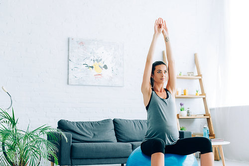 Young pregnant sportswoman training on fitness ball in living room