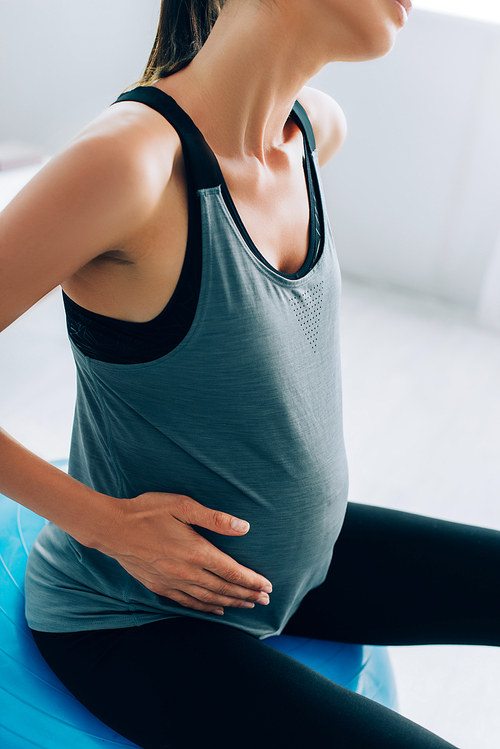 Cropped view of pregnant woman in sportswear sitting on fitness ball