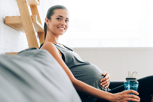 Selective focus of pregnant sportswoman  and holding sports bottle on couch