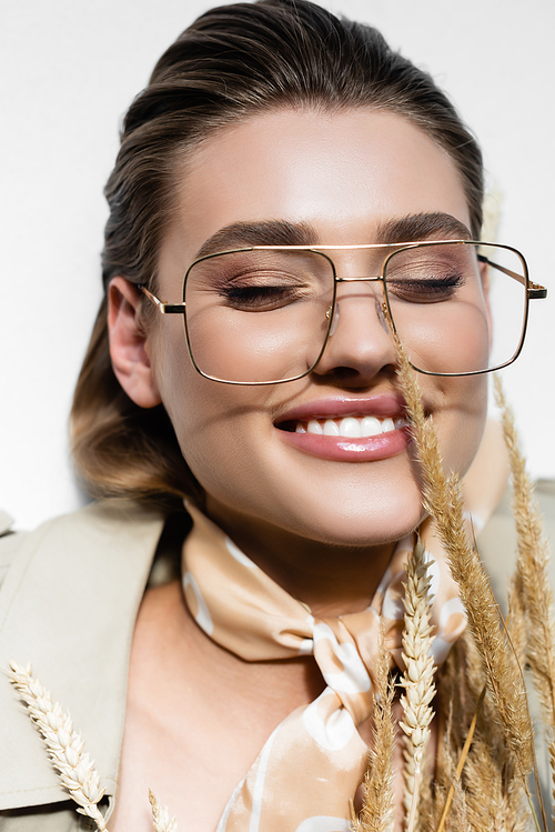 top view of happy woman in glasses and scarf lying near wheat on white