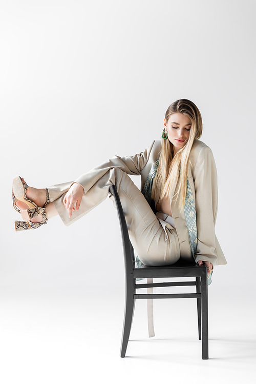 young trendy woman in suit sitting on wooden chair and looking down on white