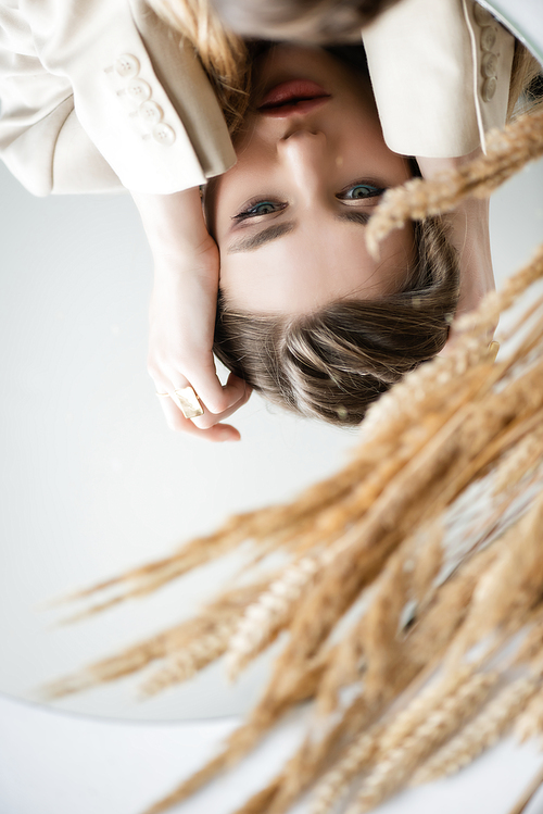 reflection of upset young woman near barley spikelets on white