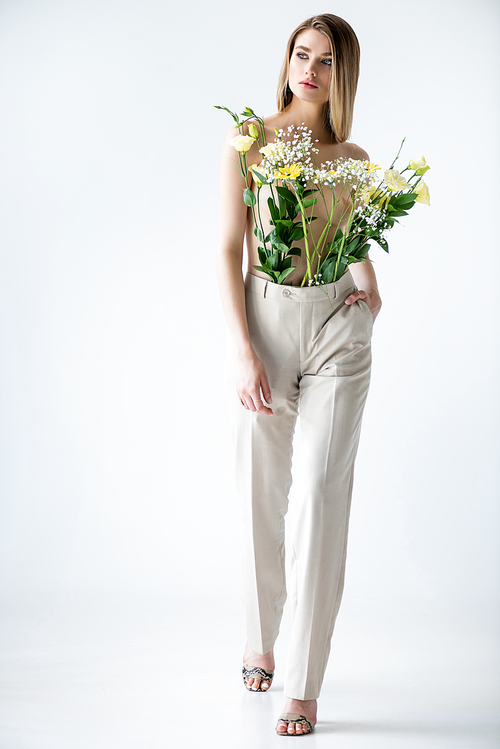 full length of young woman with flowers in pants posing on white