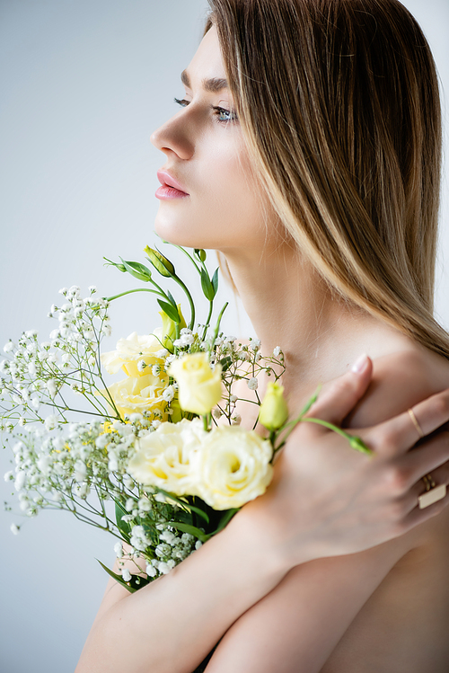 woman with naked shoulders embracing flowers on grey