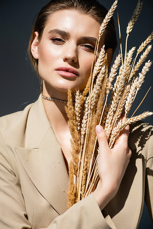 young woman in beige blazer  near wheat spikelets on dark grey