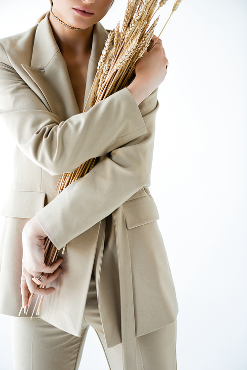 cropped view of young woman in beige blazer holding wheat on white