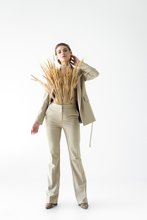 stylish woman in beige suit with wheat spikelets posing on white