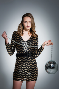 young woman in dress  while holding disco ball on grey