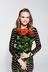 happy young woman in dress holding bouquet of red roses on grey