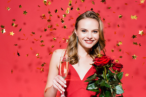 happy woman holding roses and glass of champagne near falling confetti on red