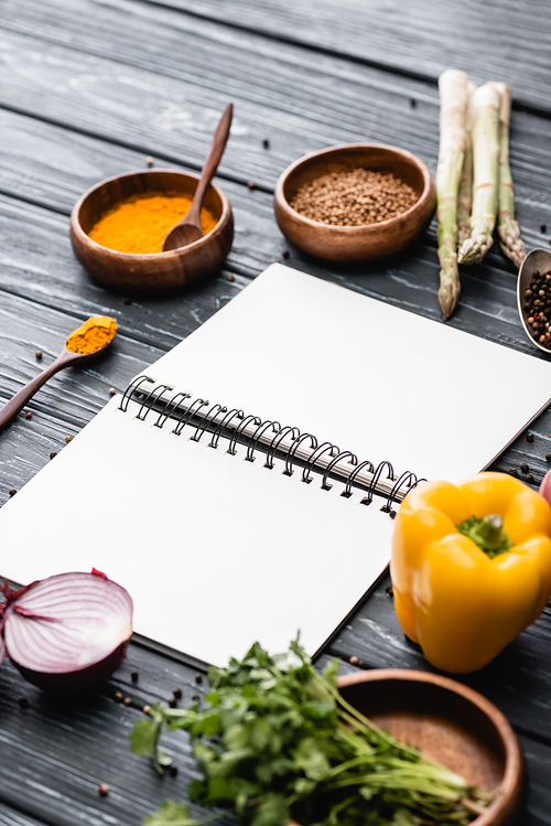 selective focus of fresh colorful vegetables and spices near blank notebook on wooden surface