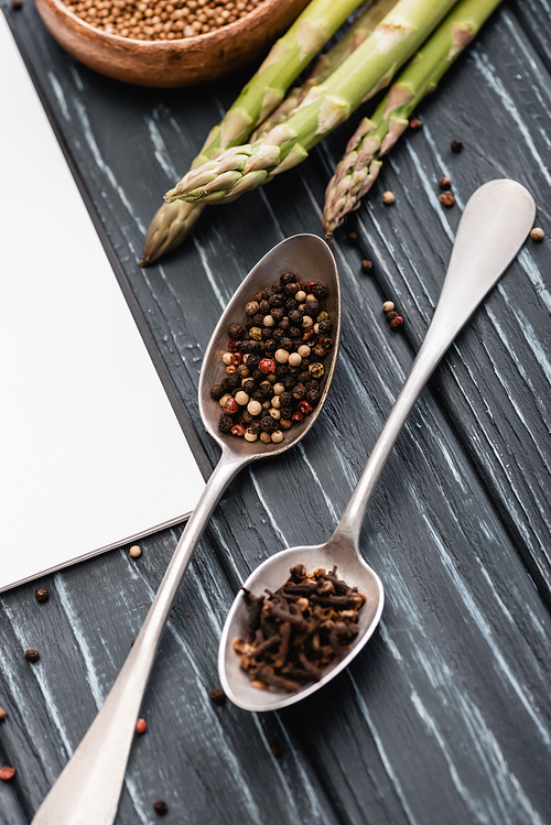 spices in spoons near asparagus on wooden surface