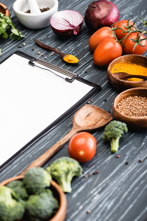 selective focus of blank clipboard near spices and vegetables on wooden surface