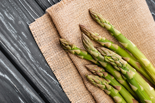 close up view of fresh green asparagus on burlap on wooden surface