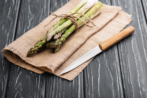fresh green asparagus on burlap with knife on wooden surface