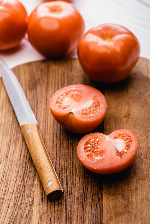 selective focus of ripe tomatoes on wooden chopping board with knife