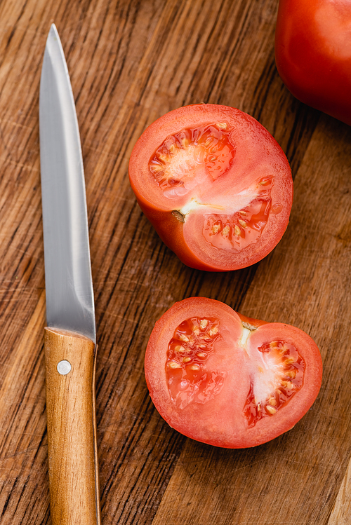 top view of ripe tomato halves on wooden chopping board with knife