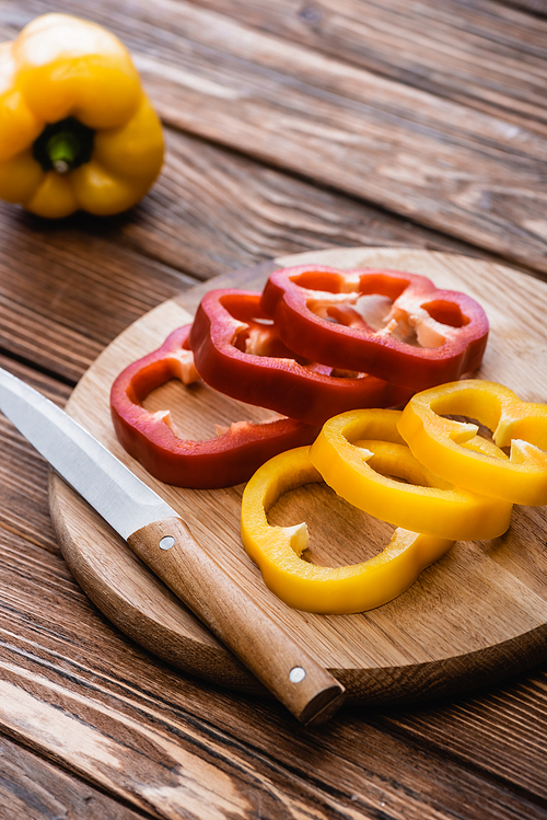 selective focus of colorful sliced bell peppers on wooden cutting board near knife
