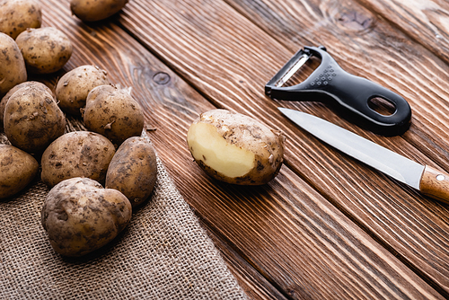 dirty potatoes on wooden table with peeler and knife