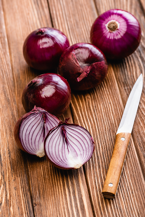 cut and whole red onion near knife on wooden table