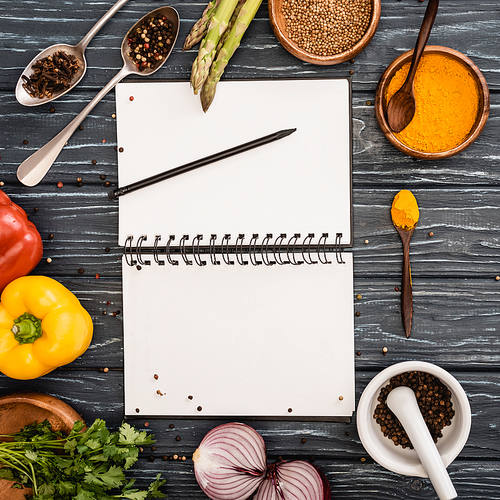 top view of fresh colorful vegetables and spices near blank notebook on wooden surface