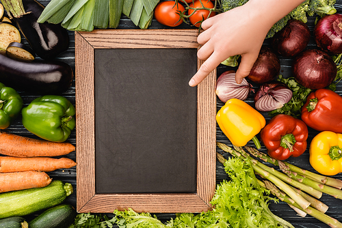 cropped view of person pointing at empty chalkboard near fresh colorful vegetables