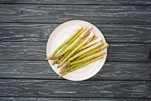 top view of fresh asparagus on plate on wooden surface