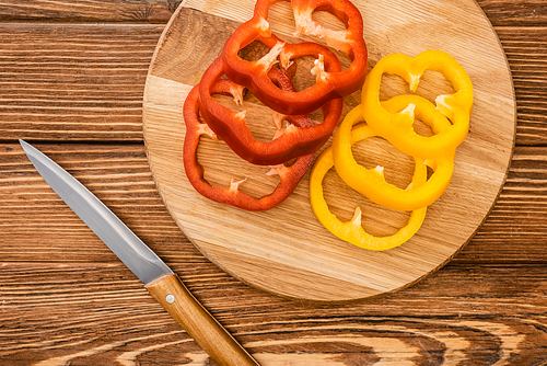 top view of colorful sliced bell peppers on wooden cutting board near knife