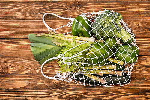 top view of fresh green ripe vegetables in string bag on wooden table