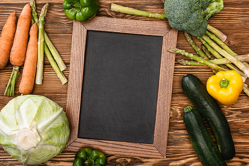 top view of fresh ripe vegetables and empty chalkboard on wooden background